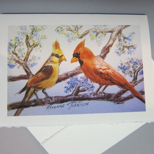 K&ouml;nnte beinhalten: Ein Aquarellbild von zwei Kardin&auml;len, die auf einem Ast mit blauen und wei&szlig;en Bl&uuml;ten sitzen. Der m&auml;nnliche Kardinal ist rot und der weibliche Kardinal ist gelb. Das Bild ist signiert mit "Roxanne Jobaison".