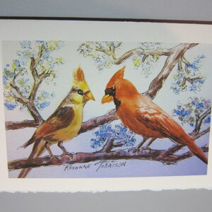 K&ouml;nnte beinhalten: Ein Aquarellbild von zwei Kardin&auml;len, die auf einem Ast sitzen. Der m&auml;nnliche Kardinal ist rot und der weibliche Kardinal ist gelb. Der Hintergrund ist hellblau mit wei&szlig;en Bl&uuml;ten.