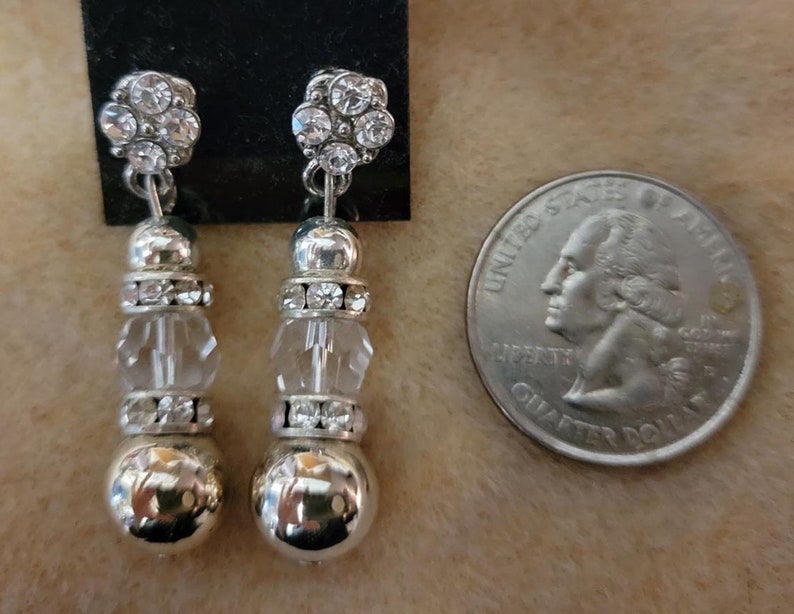 May include: A pair of silver dangle earrings with clear crystal beads and silver balls at the bottom. The earrings are about the size of a quarter.