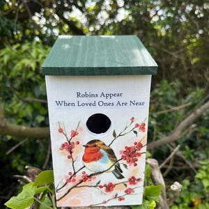 May include: A white wooden birdhouse with a green roof, decorated with a painted robin on a branch with red berries. The birdhouse has a circular entrance and the text "Robins Appear When Loved Ones Are Near".