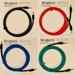 Puede incluir: Cuatro cables de audio en negro, rojo, azul y verde, cada uno con un conector de 6,35 mm. Los cables están etiquetados como "Mogami #2549" y "Assembled in Tokyo". Los cables están dispuestos en un patrón circular.