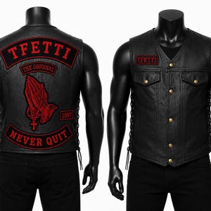 Op de afbeelding: Een zwart leren vest met een V-hals, goudkleurige drukknopen en vetersluiting aan de zijkanten. De achterkant toont rode geborduurde patches met de tekst TFETI, THE ORIGINAL, 1957, NEVER QUIT en een afbeelding van biddende handen met een kruis.