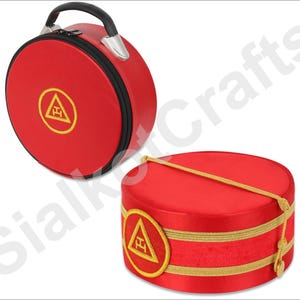 Op de afbeelding: Rode ronde koffer met een zwarte rits en handvat, en een bijpassende rode hoed. Beide items hebben een goud geborduurd embleem in een cirkel. De koffer heeft een zwart handvat en zilveren accenten. De hoed heeft gouden afwerking en een decoratief koord.