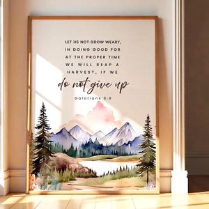 May include: Framed watercolor print featuring a mountain landscape with pine trees and a lake. The artwork includes the text "LET US NOT GROW WEARY...do not give up" from Galatians 6:9. The frame is a light brown color.