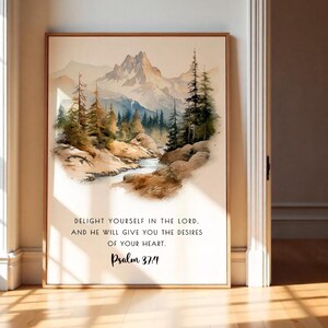 Puede incluir: Impresión artística de paisaje en acuarela con una cordillera, un río y árboles en tonos verdes, marrones y azules. La impresión incluye el texto: "DELIGHT YOURSELF IN THE LORD. AND HE WILL GIVE YOU THE DESIRES OF YOUR HEART. Salmo 37:4."