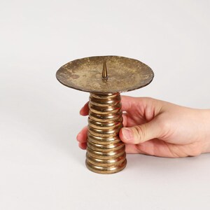 以下が含まれることがあります： 螺旋状のベースと丸いトップを持つ金色の金属製のキャンドルホルダー。ホルダーのトップの中央には小さなスパイクがあります。