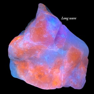 Könnte beinhalten: Ein leuchtendes, unregelmäßig geformtes Mineralpräparat vor schwarzem Hintergrund. Der Stein zeigt leuchtende Farben, darunter Orange, Rosa, Blau und Lila. Der Text "Long wave" ist sichtbar.