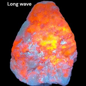 May include: A close-up of a rock that glows orange and yellow under long wave UV light. The rock has a rough, textured surface. "Long wave" is written in white text at the top of the image.