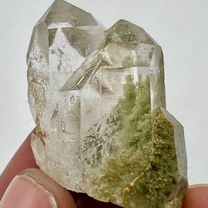 Puede incluir: Un grupo de cristales de cuarzo transparentes con inclusiones verdes. Los cristales son facetados y tienen una textura natural y rugosa.