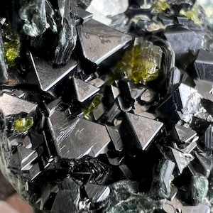 May include: Close-up of a mineral specimen featuring dark, metallic, triangular crystals. The crystals are interspersed with translucent, yellowish-green formations, creating a striking contrast. The overall texture is rough and jagged.
