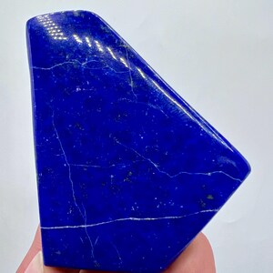 May include: A deep blue lapis lazuli crystal with white veins. The crystal is shaped like a triangle and has a smooth, polished surface.