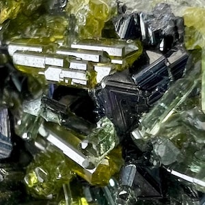 Könnte beinhalten: Nahaufnahme einer Mineralprobe mit einer Ansammlung von kristallinen Strukturen. Das Bild zeigt eine Vielzahl von Formen und Farben, darunter durchscheinendes Grün, Schwarz und Weiß, mit Fokus auf die komplizierten Details der Mineralformationen.