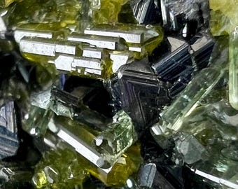 May include: Close-up of a mineral specimen featuring a cluster of crystalline structures. The image showcases a variety of shapes and colors, including translucent green, black, and white, with a focus on the intricate details of the mineral formations.