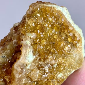 May include: Close-up of a raw, uncut citrine crystal cluster. The crystal features a golden-yellow hue with numerous small, sparkling crystal formations. The base of the crystal has a light green color.