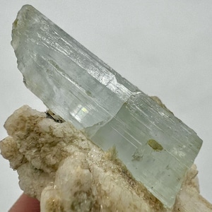 May include: A large, light green aquamarine crystal with striations on a white matrix.
