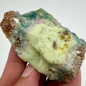 Pode incluir: Uma rocha áspera, verde e marrom com um centro verde claro. A rocha tem uma variedade de texturas e cores, incluindo marrom, verde e branco.