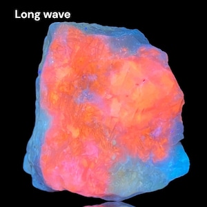 May include: A close-up of a rough, irregularly shaped rock with a bright orange, pink, and blue fluorescence under long wave UV light. The text "Long wave" is visible in the upper left corner of the image.