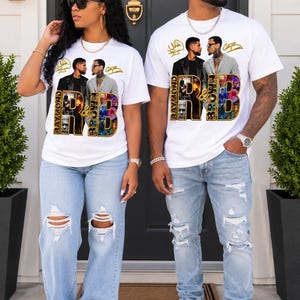 May include: A white short-sleeve t-shirt featuring a graphic print of two men, Usher and Chris Brown, with the text RAYMOND & BROWN. The design includes gold-toned lettering and small photo collages within the letters. The shirt is paired with light blue distressed denim jeans and white sneakers.
