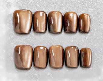 May include: A set of ten press-on nails in a glossy, metallic bronze finish. The nails are arranged in two rows of five, featuring a smooth, reflective surface with a deep brown hue and subtle light-catching highlights across each individual nail.