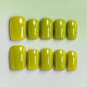 May include: A set of ten artificial nails in a vibrant, solid lime green color. The nails are square-shaped and glossy, arranged in two rows of five. The image is taken from a top-down perspective, showcasing the smooth, polished surface of the nails.