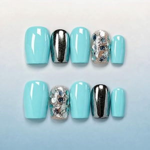 Puede incluir: Un conjunto de uñas postizas con varios diseños. Las uñas presentan un diseño azul claro, plateado cromado y con purpurina. Las uñas son de forma ovalada y están dispuestas en dos filas de cinco.