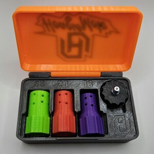 May include: An open orange and black case containing three multi-colored nozzles and a black knob. The nozzles are green, red, and purple. The case lid has the text "Hoop Hops" and a logo.