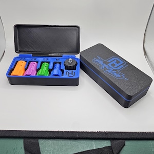 May include: A black and blue tool kit with a variety of colored attachments. The kit includes orange, purple, green, and blue pieces, along with a black piece. The lid of the kit has the text "House Moto" in blue.