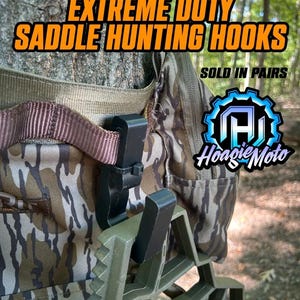 May include: Camouflage hunting saddle with the text "EXTREME DUTY SADDLE HUNTING HOOKS" in orange and black. The image shows a close-up of the saddle's hooks and straps, with the brand logo "Hoagie Moto" in the bottom right corner.