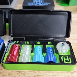 May include: A black and green 3D-printed storage case with a hinged lid, containing several colorful nozzles. The nozzles are red, clear, light blue, and dark blue, with sizes labeled 22, 20, 18, and 16. A clear, star-shaped piece is also included.
