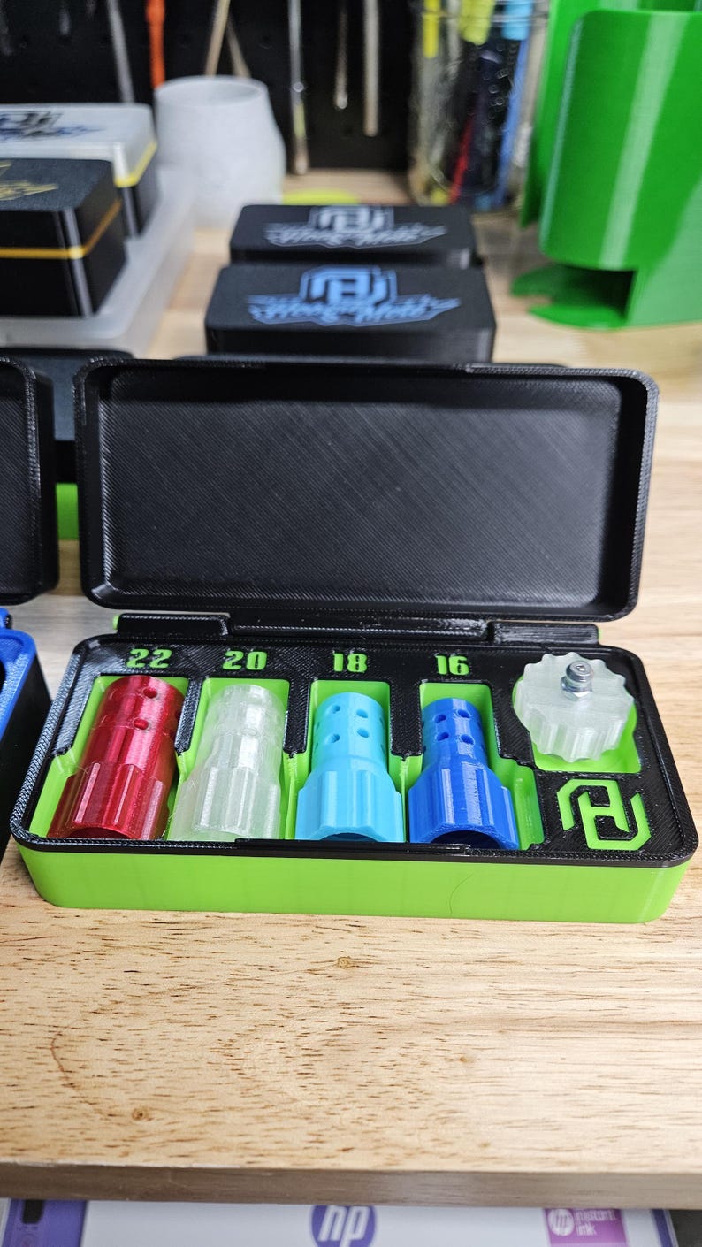 May include: A black and green 3D-printed storage case with a hinged lid, containing several colorful nozzles. The nozzles are red, clear, light blue, and dark blue, with sizes labeled 22, 20, 18, and 16. A clear, star-shaped piece is also included.
