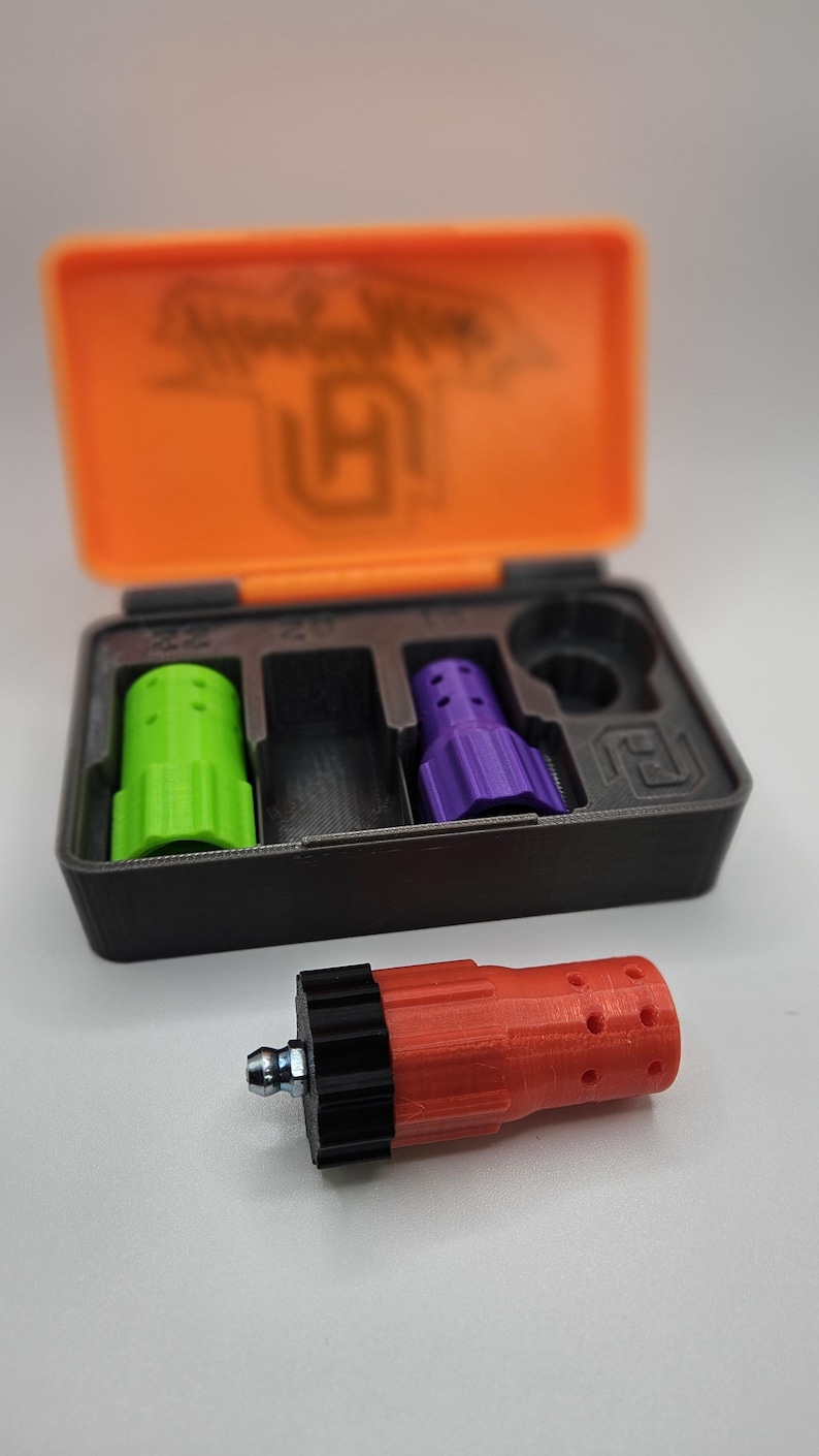 May include: A set of 3D-printed accessories in a black and orange case. The case contains a green, a black, and a purple piece. A red piece with a black end and a metal fitting is in front of the case.