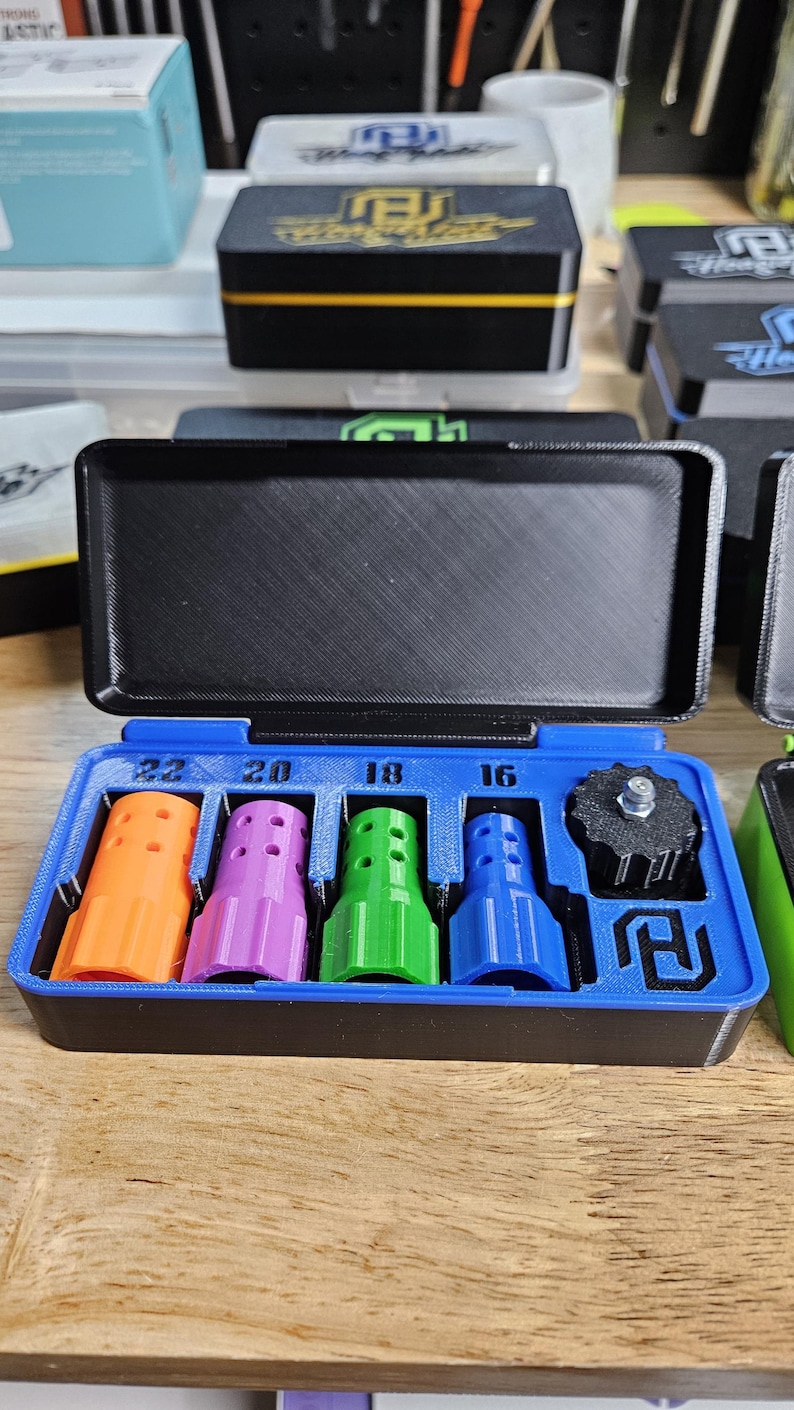 May include: A blue and black case with an open lid, containing four colorful, cylindrical objects in orange, purple, green, and blue. The case also holds a black, circular object. Numbers 16, 18, 20, and 22 are printed above the objects.