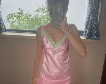 May include: A pink satin slip dress with a green and white lace trim. The dress has a strawberry design on the front.
