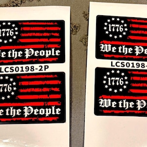 May include: Four rectangular stickers on white backing paper, each featuring a black background with red horizontal stripes, a circle of white stars, the year 1776, and the text We the People. The code LCS0198-2P is printed between the stickers.