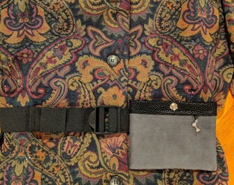 May include: A black fabric belt with a silver buckle and a gray fabric pouch with a silver charm attached. The belt is worn over a dark blue and gold paisley patterned fabric.