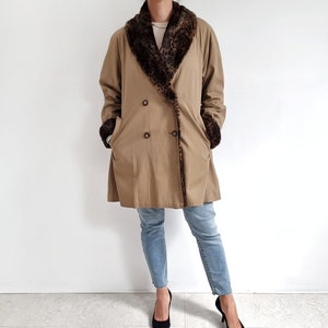 May include: A tan double-breasted coat with a leopard print faux fur collar and cuffs. The coat is worn over blue jeans and black heels.
