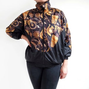 May include: A black and gold patterned jacket with a zip closure. The jacket has a stand-up collar and long sleeves.
