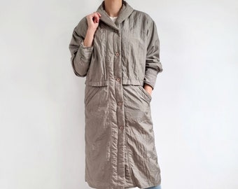 May include: A long, gray quilted coat with a button-up front and a collar. The coat has a cinched waist and pockets on the front.