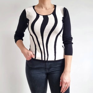 Pode incluir: Camisola de manga comprida com riscas pretas e brancas e decote redondo.