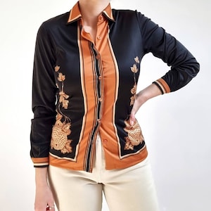 May include: A black and orange long-sleeved shirt with a floral pattern. The shirt has a button-up front and a collar.