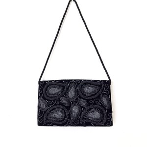 May include: A black velvet evening bag with a silver paisley design. The bag has a long strap.