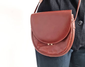 May include: A brown leather satchel bag with a curved flap and a gold clasp. The bag is worn over the shoulder and has a long strap.