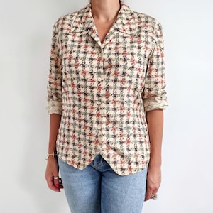 May include: A cream-coloured button-down shirt with a houndstooth pattern in shades of red, blue, and black. The shirt has a collared neckline and long sleeves.