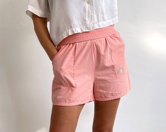 Puede incluir: Shorts de algodón rosa con una cintura elástica ancha y un pequeño parche bordado en el lado derecho.