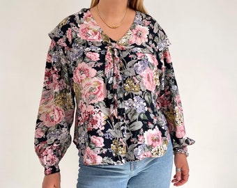 May include: A black and white floral print blouse with a ruffled collar and long sleeves. The blouse has a tie at the neck and a button closure.