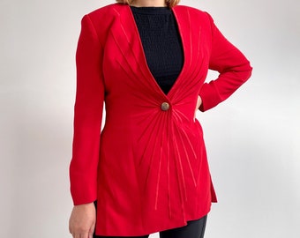 Puede incluir: Una chaqueta roja con un diseño único con un patrón de rayos de sol. La chaqueta tiene un cierre de botón único y mangas largas.