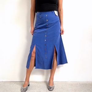 May include: A blue midi skirt with a button front and side slits. The skirt is made of a smooth, silky fabric.