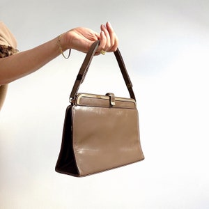 May include: A brown leather handbag with a gold clasp and a top handle. The bag is rectangular in shape and has a smooth finish.