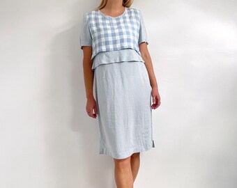 May include: A light blue dress with a gingham pattern. The dress has a short sleeve and a layered skirt.