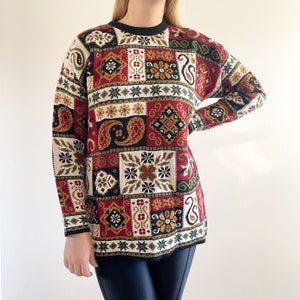 Könnte beinhalten: Ein rot-weiß-grün-schwarzer Pullover mit Rundhalsausschnitt. Der Pullover hat ein geometrisches Muster mit Paisley- und Blumenmotiven.